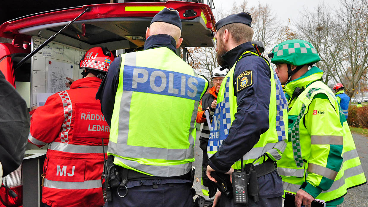 Personal från räddningstjänsten, polisen och ambulanssjukvården står tillsammans vid en ledningsbuss och tittar på information på en white board-tavla.