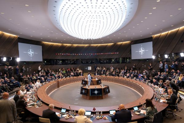 Mötesrum i Nato. En person står i mitten och omgärdas av massa folk. 