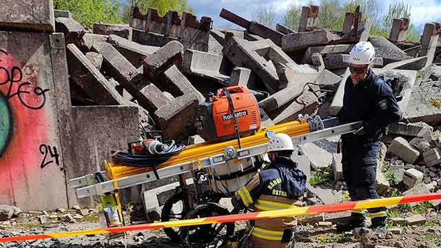 Två personer framför en raserad byggnad.