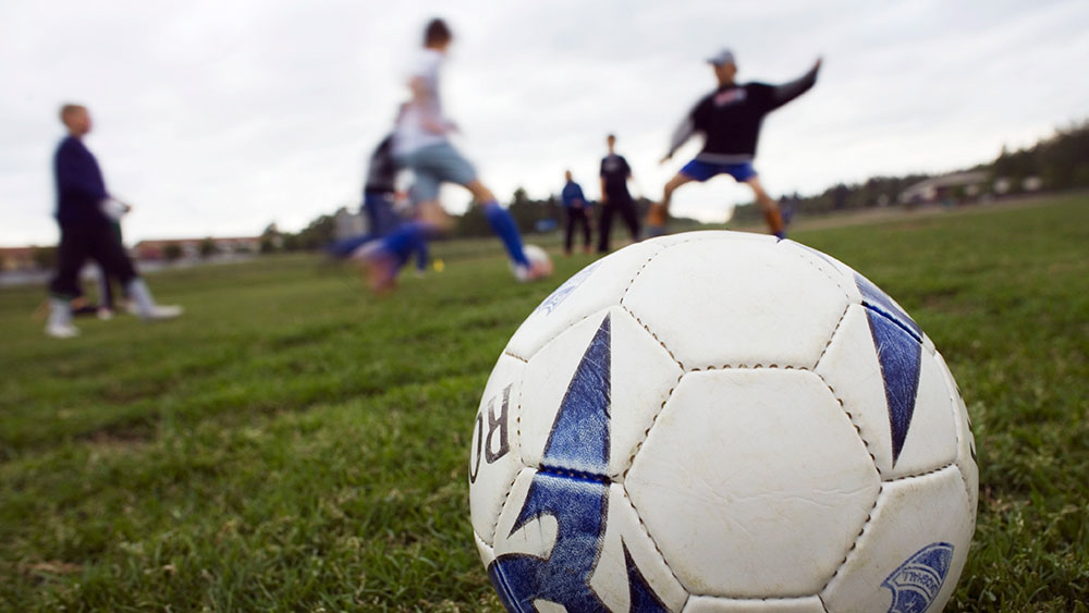 Fotbollstränande killar i bakgrunden, inzoomad fotboll i förgrunden.