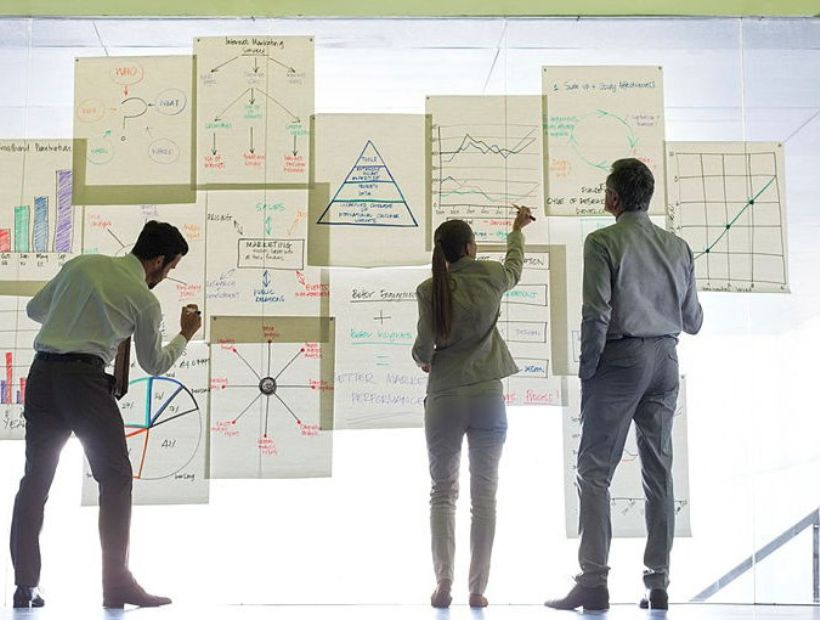 Två män och en kvinna står framför en vägg med grafer och tabeller framför sig.