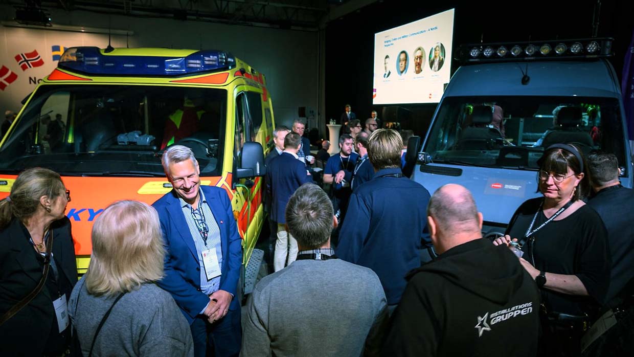 Mässbesökare minglar i anslutning till en ambulans och ett ledningsfordon i en mässhall.