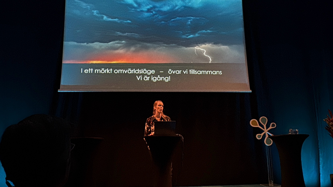 Projektledare Sofie Ivarsson står på en scen och beskriver scenariot från Övning av totalförsvar (ÖTF) under Mötesplats samhällsäkerhet.