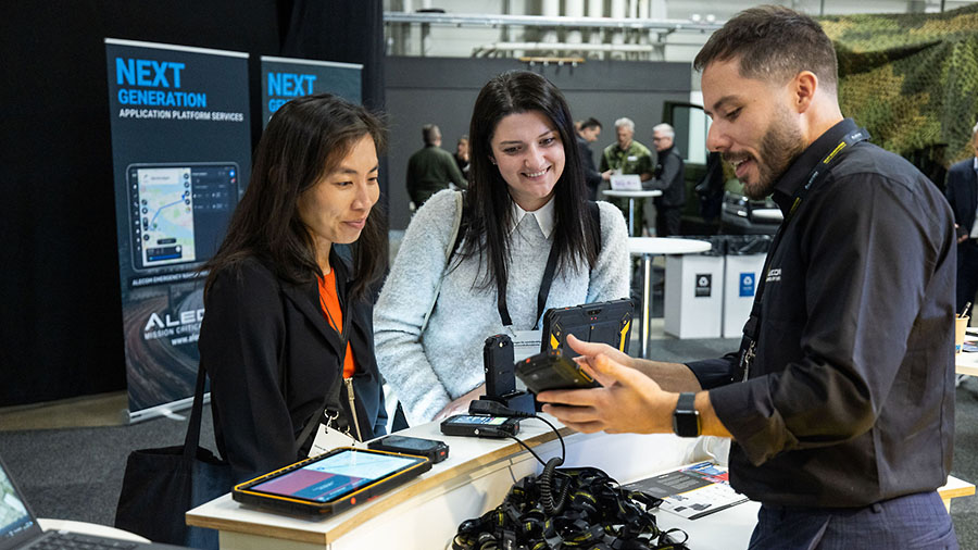 Två mässbesökare talar med en säljare som visar telekomutrustning.