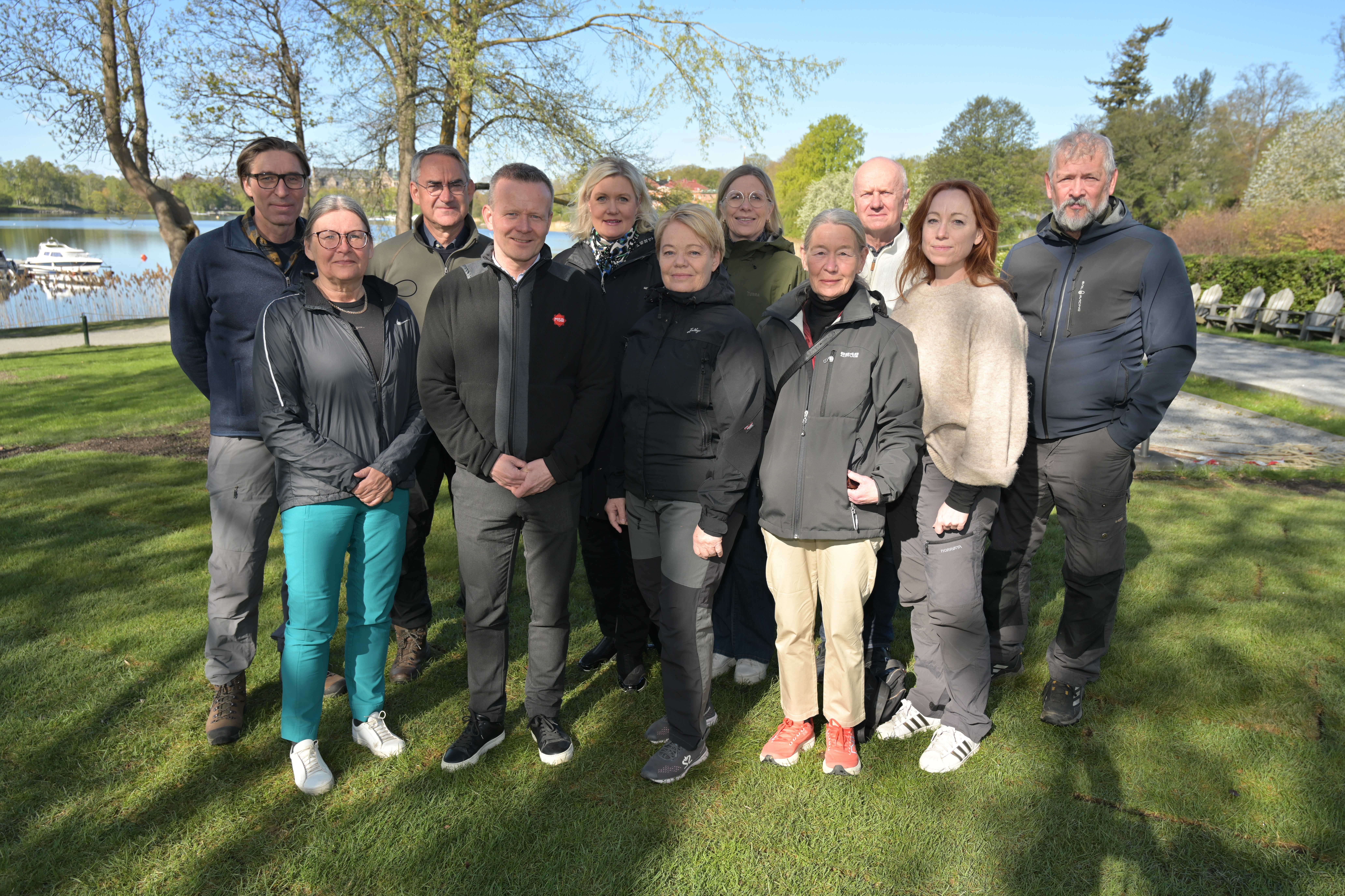 Människor står tillsammans på en gräsmatta framför ett träd