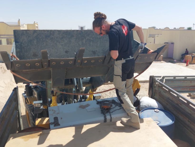 En man står och lastar av saker på en grävskopa.