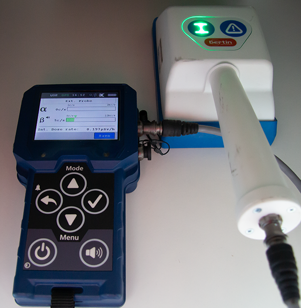 Mätinstrument med tillkopplad extern mätprob för detektering av alfa (α) och beta (β) strålning. På instrumentets display visas värden för uppmätt nivå som värde och graf. I displayen visa även nuvarande doshastighet för gamma (γ) strålning.